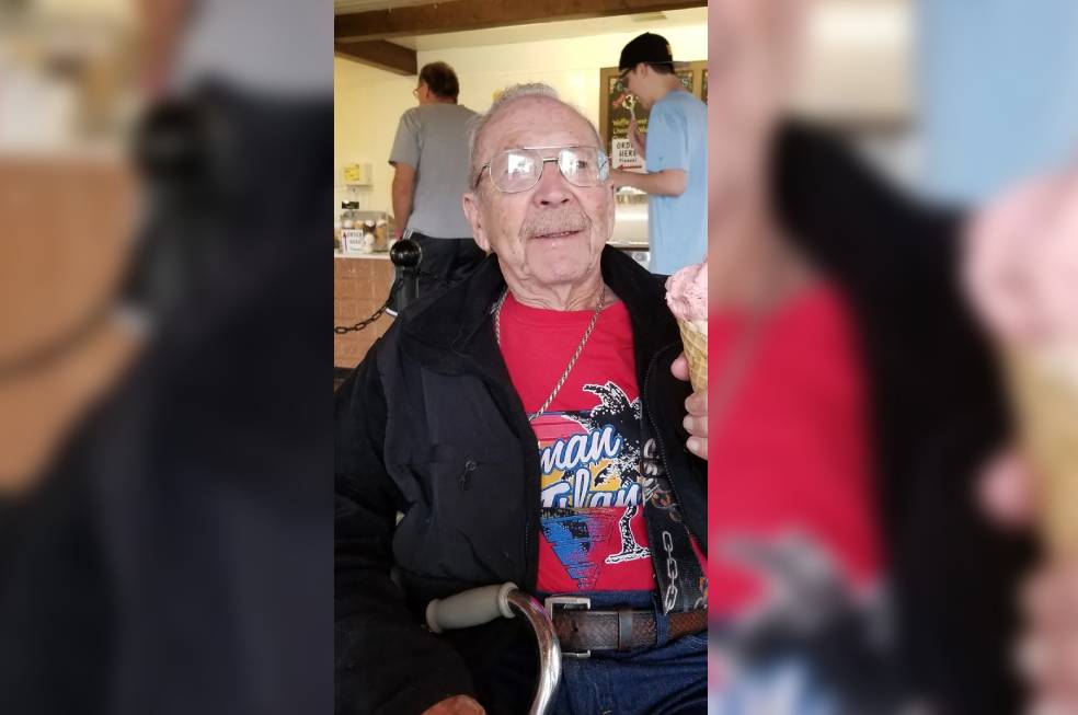 An old man wearing a black jacket sitting and having ice cream