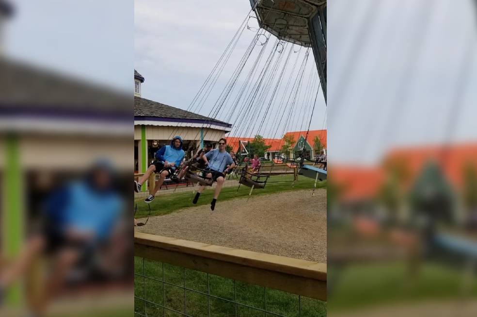 Two men swinging on a ride in a park wearing white